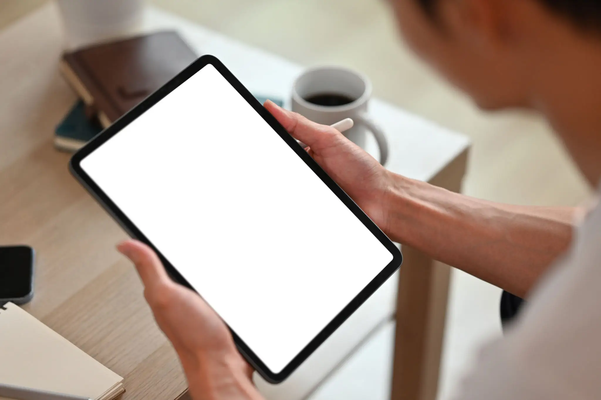 Person holding a tablet with a blank screen near a coffee cup.