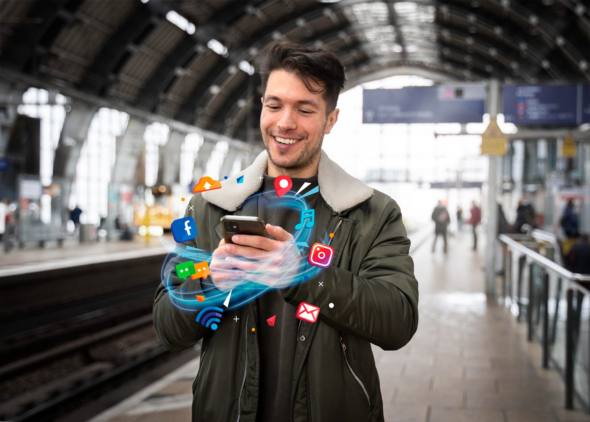 Young man happily using his smartphone at a train station, with colorful digital icons around.